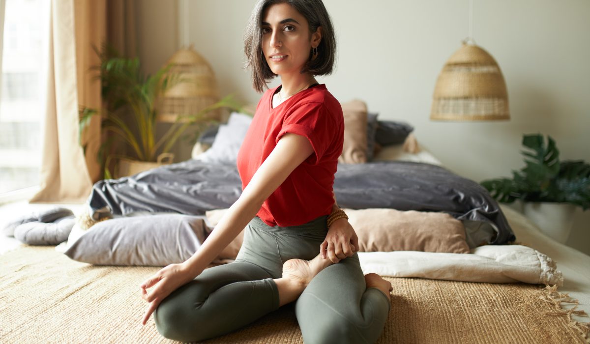Beautiful gray haired young woman in activewear sitting in half lord of fishes posture or ardha matsyendrasana, doing seated spinal twist during yoga practice indoors. Wellbeing and healthy lifestyle
